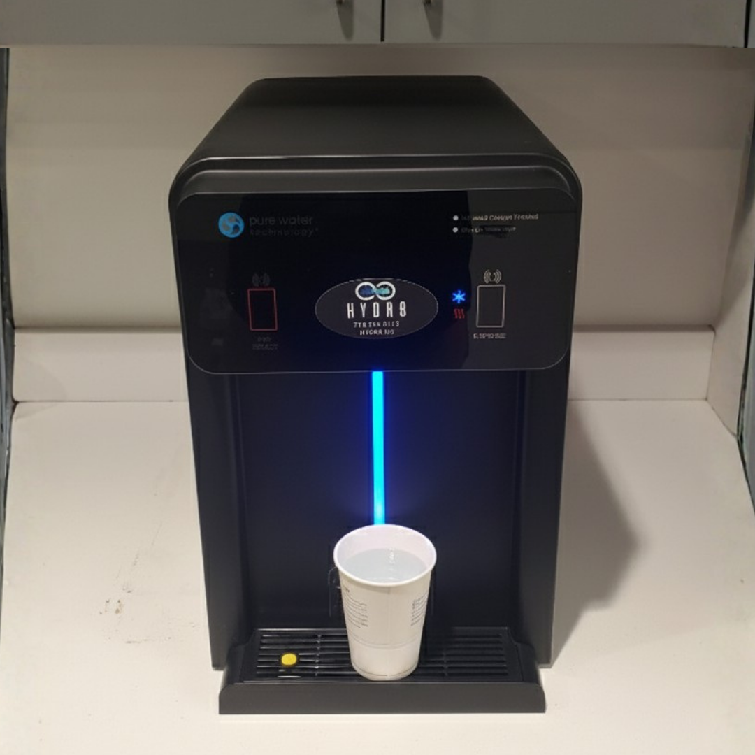 Black water dispenser with a white cup underneath on a light-colored countertop.