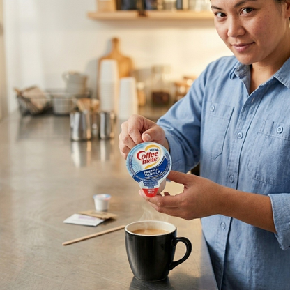 Person adding Coffee mate French Vanilla creamer to a black mug of coffee in a breakroom