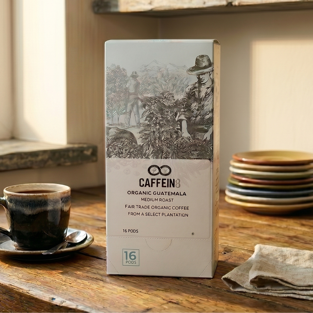 CAFFEIN8 Organic Guatemala 16-pod box on a rustic wood table with a cup of coffee and stacked plates