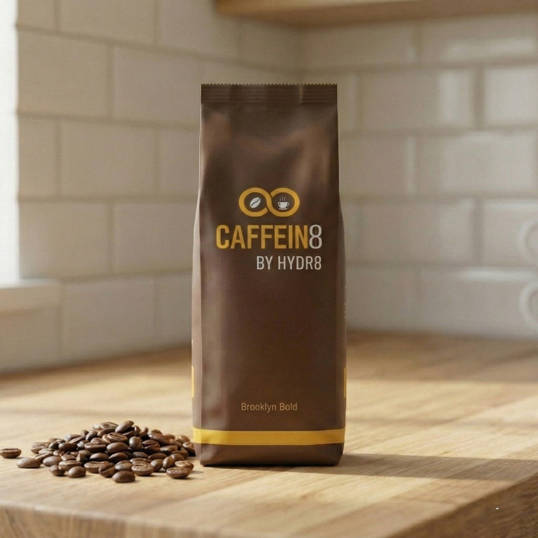 Caffein8 by Hydr8 Brooklyn Bold dark roast coffee bag on a wooden countertop with scattered coffee beans and white tile backsplash