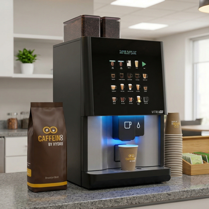 Caffein8 by Hydr8 Brooklyn Bold coffee bag beside a Vitro X5 commercial bean-to-cup machine with a branded cup in an office kitchen setting