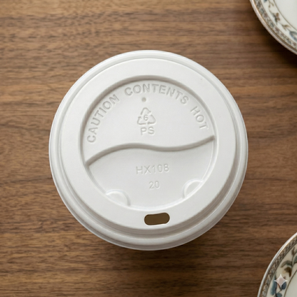 White hot coffee cup lid, model HX108, on a wood table beside dishware