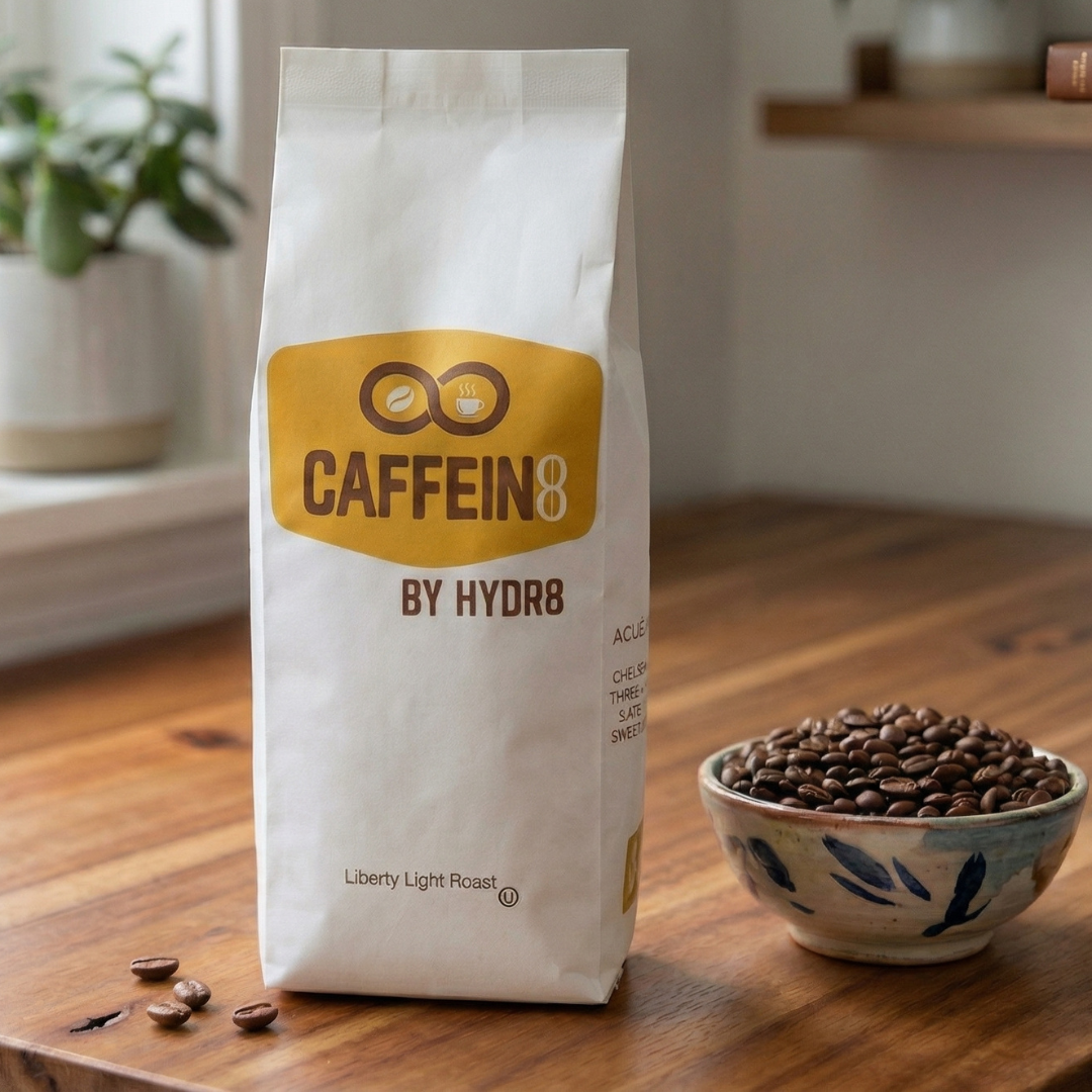 CAFFEIN8 by HYDR8 Liberty Light Roast whole bean coffee bag on wood table with fresh roasted coffee beans in ceramic bowl