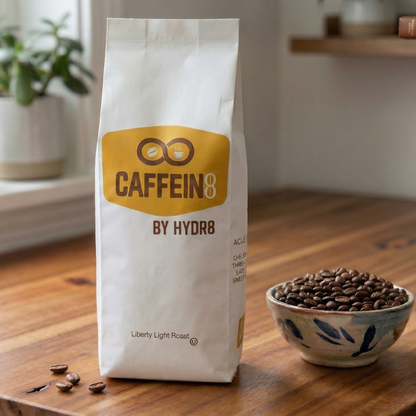 CAFFEIN8 by HYDR8 Liberty Light Roast whole bean coffee bag on wood table with fresh roasted coffee beans in ceramic bowl