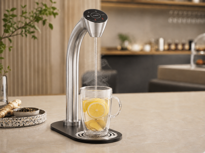 HYDR8 countertop water tap dispensing steaming hot water into a glass mug with lemon and ginger on a break room counter
