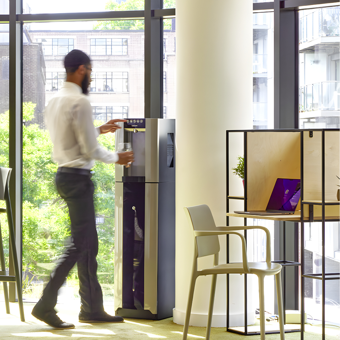 Person filling a bottle at a HYDR8 premium freestanding water dispenser in a bright modern office