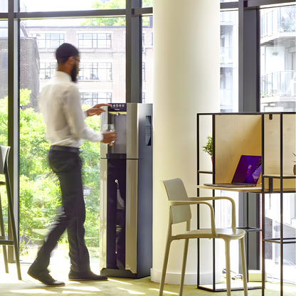 Person filling a bottle at a HYDR8 premium freestanding water dispenser in a bright modern office